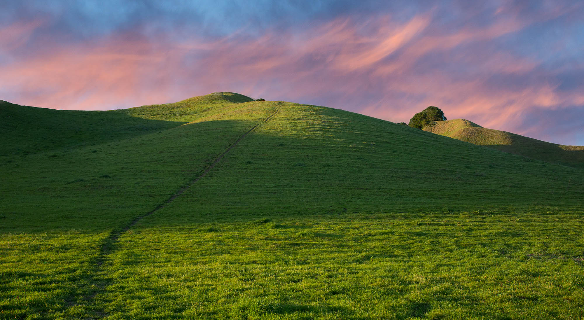 17241885306_0c3e1b8d8e_o.jpg Green grassy hill with path to the top and blue sky with pink clouds
